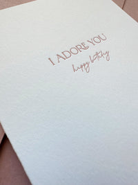 Close-up of letterpress “I Adore You” text in dusty rose ink on bright white cotton cardstock
