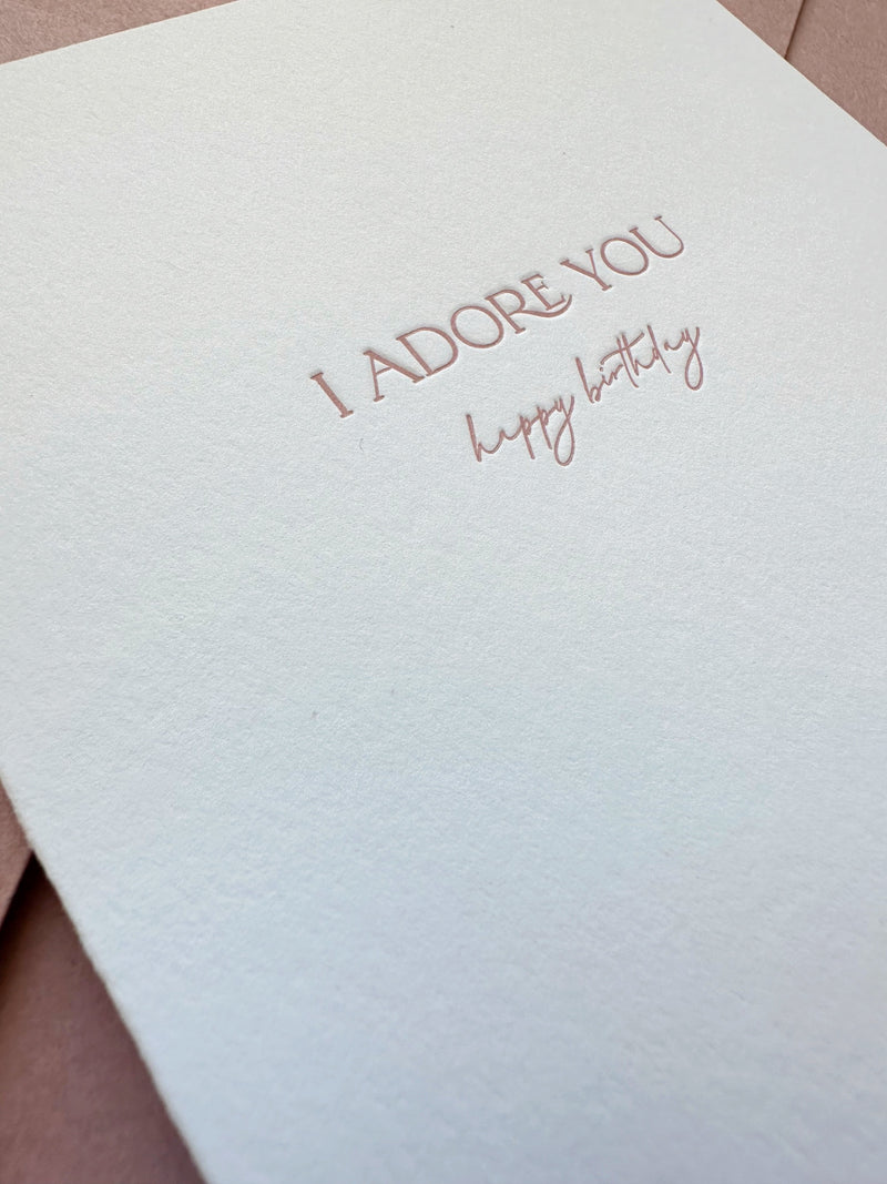 Close-up of letterpress “I Adore You” text in dusty rose ink on bright white cotton cardstock
