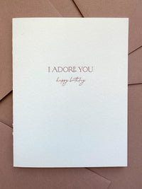 Letterpress birthday card with “I Adore You” text in dusty rose ink on bright white cotton cardstock, paired with a dusty rose envelope