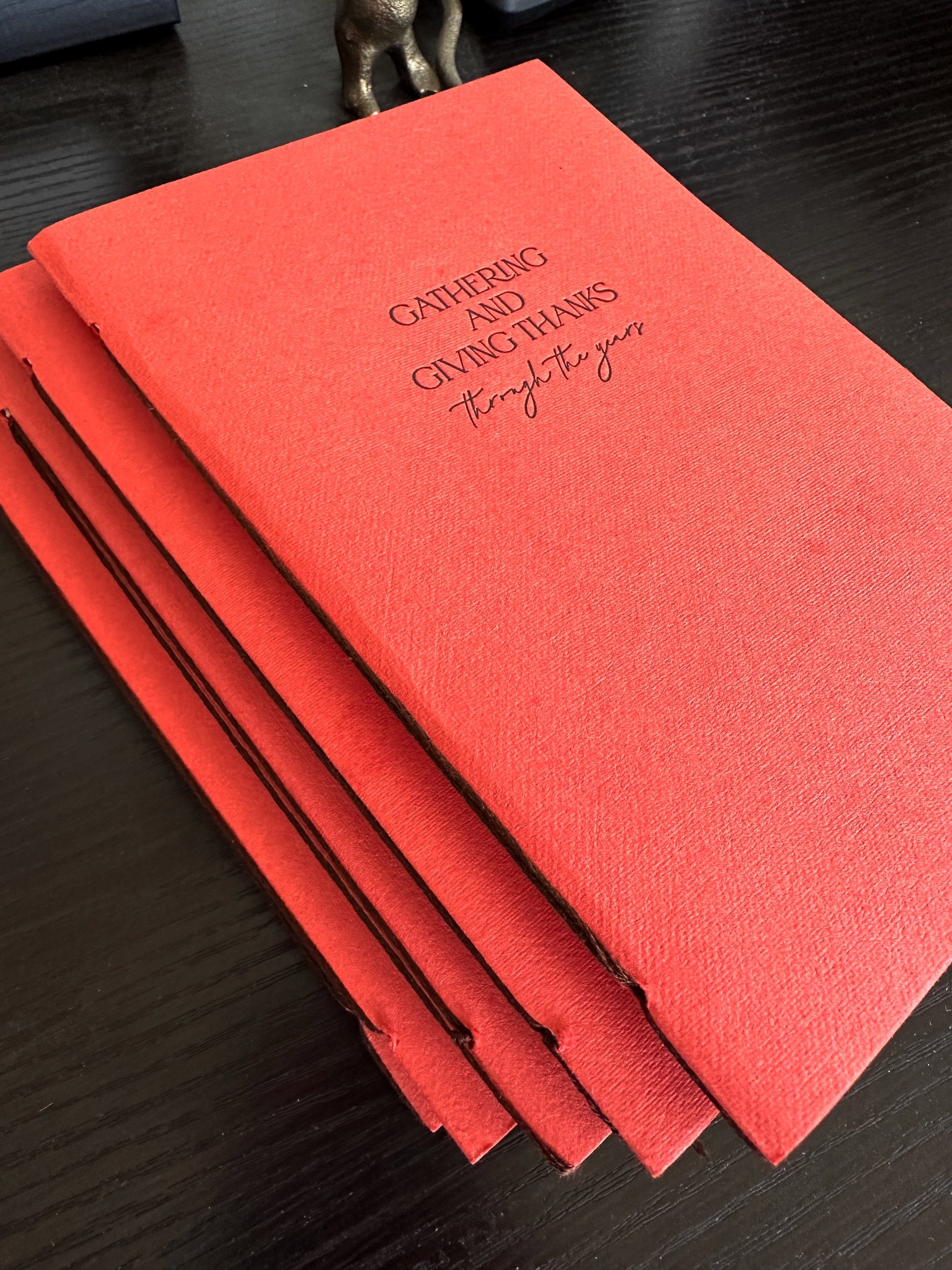 Overhead angled view of hand-bound Thanksgiving journal with persimmon handmade paper cover and letterpress chocolate ink text