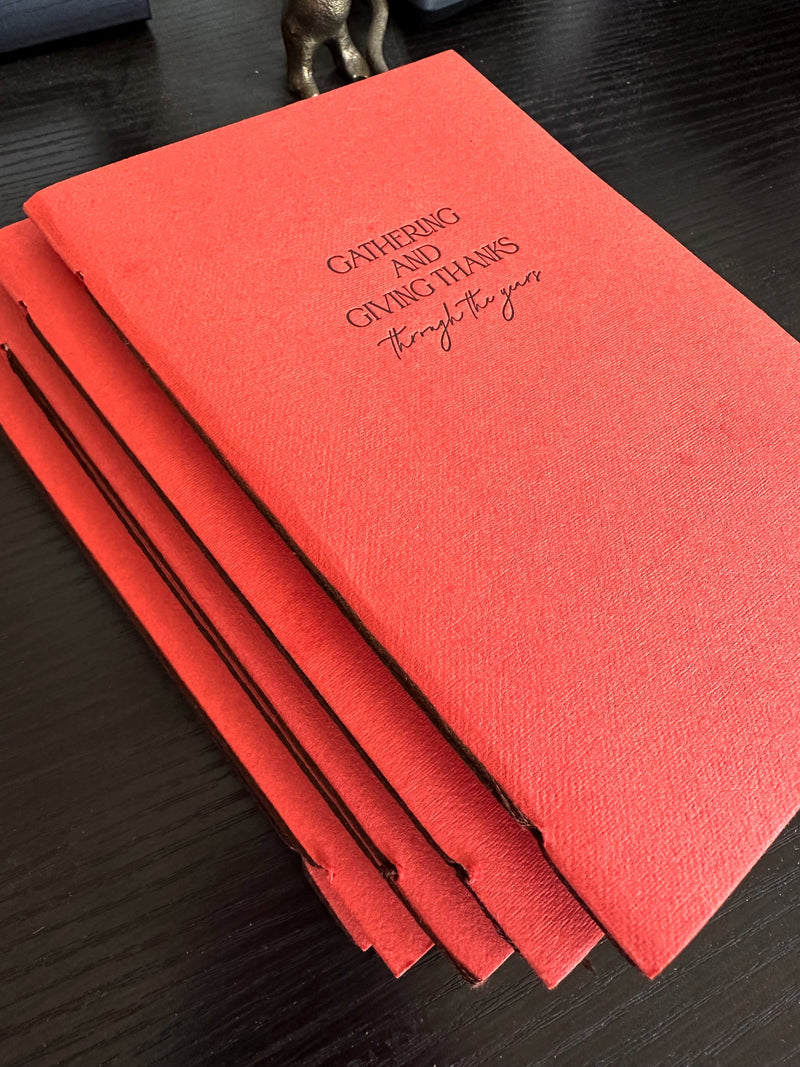 Overhead angled view of hand-bound Thanksgiving journal with persimmon handmade paper cover and letterpress chocolate ink text